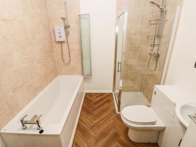 A bathroom with a bathtub a shower enclosure a toilet and a sink with wooden flooring at 1 The Warren in Robeston Wathen near Narberth