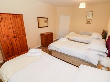 A bedroom with three single beds a wooden wardrobe a chest of drawers and a mirror at 1 The Warren in Robeston Wathen near Narberth