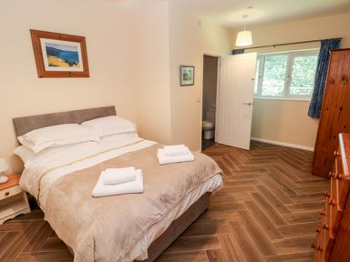 A bedroom with a bed, bedside table with lamp, wooden dresser, open door to a bathroom and window with curtains at 1 The Warren in Robeston Wathen near Narberth