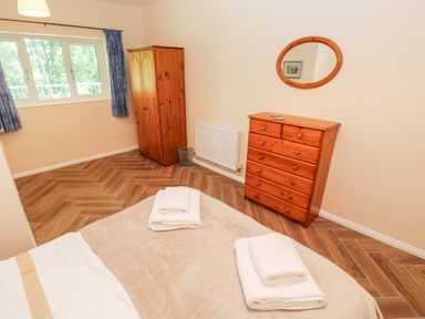 A bedroom with a bed with folded towels a wooden wardrobe a wooden dresser and an oval mirror on the wall at 1 The Warren Robeston Wathen near Narberth