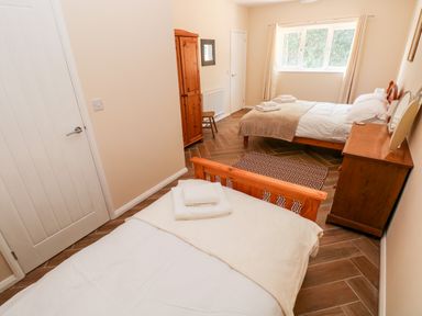 A bedroom with two wooden beds a wooden wardrobe a chest of drawers and a window at 1 The Warren in Robeston Wathen near Narberth