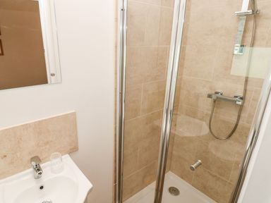 A bathroom with a sink and glass shower enclosure with beige tiled walls at 1 The Warren in Robeston Wathen near Narberth