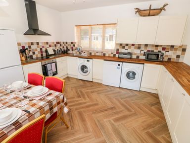 A kitchen with white cabinets wooden countertops a dining table with red chairs and kitchen appliances at 1 The Warren Robeston Wathen near Narberth