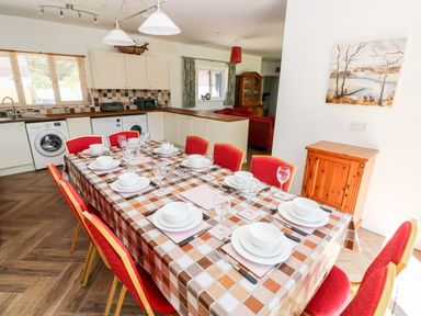 A kitchen with a dining table set for eight with red chairs and kitchen appliances at 1 The Warren Robeston Wathen near Narberth