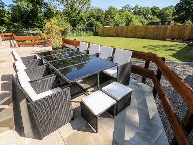 An outdoor patio with a black glass table and wicker chairs with white cushions at 1 The Warren Robeston Wathen near Narberth