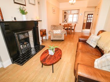 A living room with a leather sofa, armchair, wooden coffee table with a plant, black fireplace and dining table at Number 91 in Belfast County Antrim