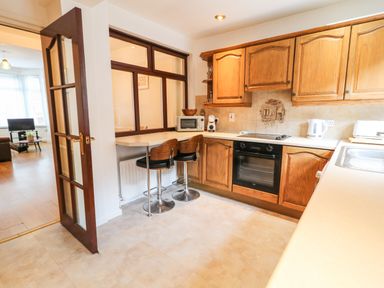 A kitchen with wooden cabinets a built in oven a microwave toaster and kettle two bar stools and a door leading to a living room at Number 91 Belfast County Antrim