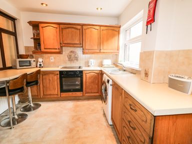 A kitchen with wooden cabinets a countertop sink washing machine oven microwave and stools at Number 91 in Belfast County Antrim