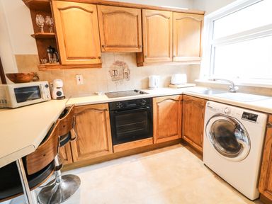 A kitchen with wooden cabinets a washing machine a microwave a kettle a toaster and two bar stools at Number 91 in Belfast County Antrim