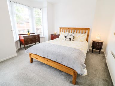 A bedroom with a wooden bed frame a bed with pillows and a blanket two wooden bedside tables with lamps and a chest of drawers by the window at Number 91 in Belfast County Antrim