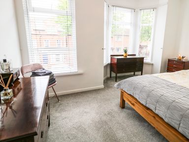 A bedroom with a wooden bed frame a desk chair beside a window and wooden dressers at Number 91 in Belfast County Antrim