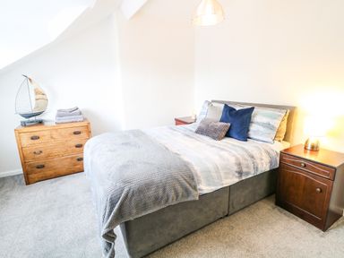 A bedroom with a bed pillows nightstand with lamp and a wooden chest of drawers with towels and a sailboat model at Number 91 in Belfast County Antrim