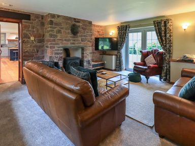 A living room with leather sofas a stone fireplace a red armchair and a wall mounted TV at Flaska House in Troutbeck Near Penrith