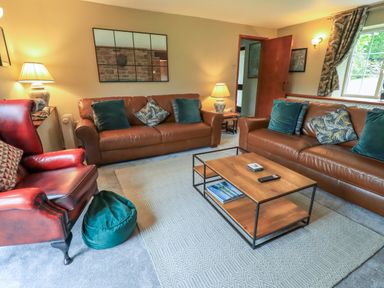 A living room with brown leather sofas a red leather armchair and a wooden coffee table at Flaska House in Troutbeck Near Penrith