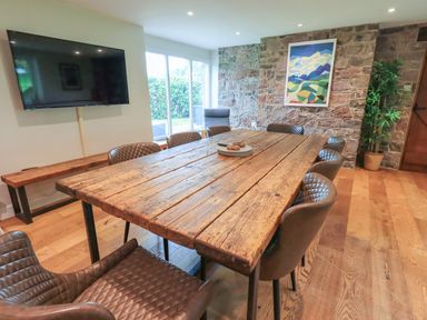 A dining room with a large wooden table surrounded by brown chairs and a wall-mounted TV at Flaska House Troutbeck Near Penrith
