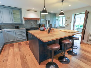 A kitchen with blue cabinets a wooden island and three stools at Flaska House in Troutbeck Near Penrith