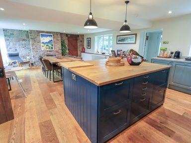 A kitchen with a wooden island and dining table near a stone wall at Flaska House Troutbeck Near Penrith