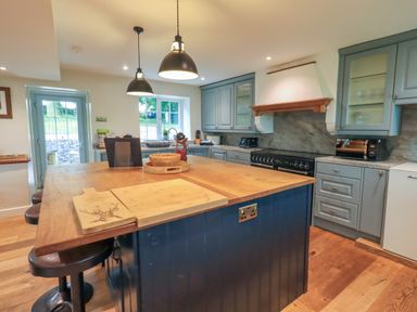 A kitchen with a wooden island and stools with blue cabinets and a window at Flaska House Troutbeck Near Penrith