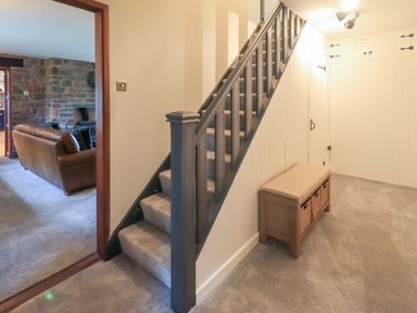 A hallway with carpeted stairs and a bench with storage baskets at Flaska House in Troutbeck Near Penrith