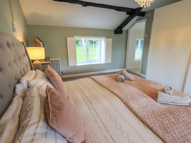 A bedroom with a bed pillows and towels on the bed a window with shutters and a bedside lamp at Flaska House in Troutbeck Near Penrith