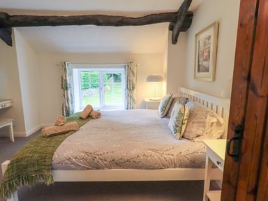 A bedroom with a bed with floral bedding and pillows by a window with curtains and a bedside table and lamp at Flaska House in Troutbeck Near Penrith