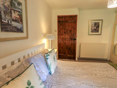 A bedroom with a white bed frame pillows a wooden door a radiator lamp and framed pictures at Flaska House in Troutbeck Near Penrith