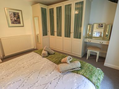 A bedroom with a bed and towels at the foot of the bed a wardrobe with checked panels and a dressing table with a stool at Flaska House Troutbeck Near Penrith