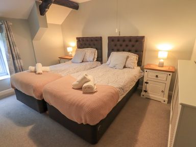 A bedroom with two single beds side by side each with towels placed on the foot of the bed and a nightstand with a lamp on either side at Flaska House in Troutbeck Near Penrith
