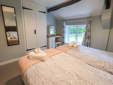 A bedroom with two beds with patterned bedding towels on top a vanity desk with a mirror a window and a full length mirror on the wall at Flaska House in Troutbeck Near Penrith