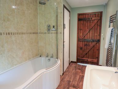 A bathroom with a bathtub shower combo tiled walls wooden door and sink at Flaska House in Troutbeck Near Penrith