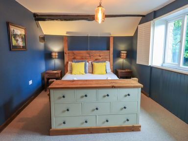 A bedroom with a wooden bed frame yellow pillows two bedside tables with lamps and a chest of drawers at Flaska House Troutbeck Near Penrith