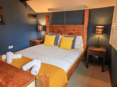 A bedroom with a wooden bed frame and yellow and gray pillows at Flaska House in Troutbeck Near Penrith