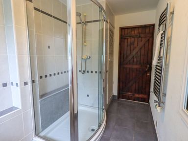 A bathroom with a curved glass shower enclosure a wooden door and a towel radiator at Flaska House Troutbeck Near Penrith