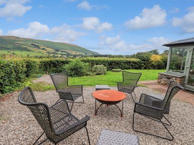 An outdoor seating area with four metal chairs around a round fire pit on gravel at Flaska House in Troutbeck Near Penrith