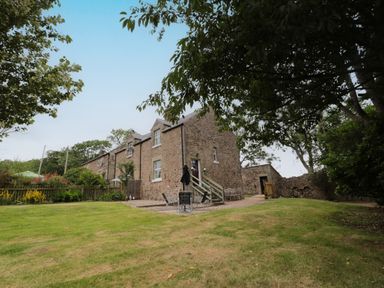 A stone house with a lawn and patio furniture surrounded by trees at 1 Roddam Rigg Cottage in Roddam near Wooler