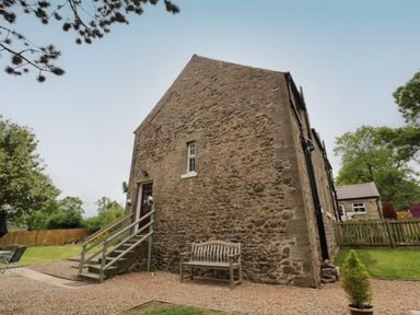 A stone cottage with steps leading to a door and a bench outside at 1 Roddam Rigg Cottage in Roddam near Wooler