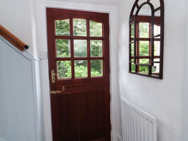 An interior hallway with a wooden door with glass panels a wall mirror and a radiator at 1 Roddam Rigg Cottage Roddam near Wooler