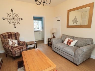 A living room with a plaid armchair and a grey sofa with animal print cushions at 1 Roddam Rigg Cottage in Roddam near Wooler