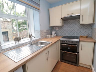A kitchen with a sink under a window and a stove with cabinets at 1 Roddam Rigg Cottage Roddam near Wooler