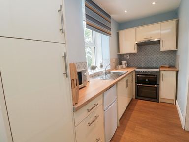 A kitchen with white cabinets a stove a sink a microwave and a window with a striped blind at 1 Roddam Rigg Cottage Roddam near Wooler