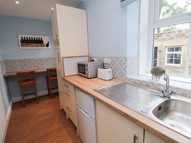 A kitchen with a sink a microwave a toaster a small fridge wooden chairs at a counter and a window at 1 Roddam Rigg Cottage Roddam near Wooler