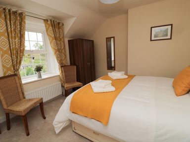 A bedroom with a bed with orange bedding two chairs a wardrobe and a window with yellow patterned curtains at 1 Roddam Rigg Cottage Roddam near Wooler