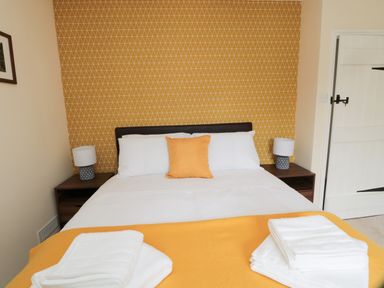 A bedroom with a bed with white linens and an orange pillow against a patterned orange wall at 1 Roddam Rigg Cottage in Roddam near Wooler