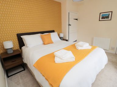 A bedroom with a double bed white bedding yellow blanket and cushion bedside tables with lamps at 1 Roddam Rigg Cottage in Roddam near Wooler