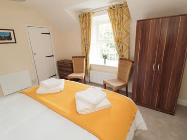 A bedroom with a bed covered by a yellow blanket and towels on top two wicker chairs near a window with yellow patterned curtains a wooden wardrobe and a chest of drawers at 1 Roddam Rigg Cottage Roddam near Wooler