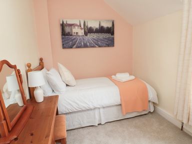 A bedroom with a single bed white bedding orange throw and wooden dressing table with lamp at 1 Roddam Rigg Cottage Roddam near Wooler
