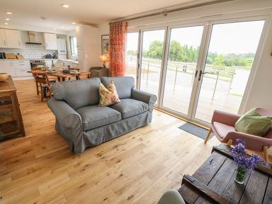 An open plan living room and kitchen with a grey sofa, wooden dining table with chairs, sliding glass door leading outside, and kitchen with white cabinets at Syrah in Seaview