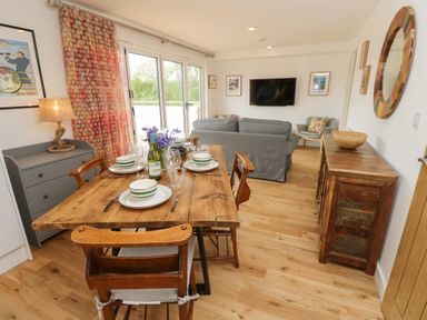 A dining area with a wooden table set for four next to a living room with a sofa and wall-mounted TV at Syrah in Seaview
