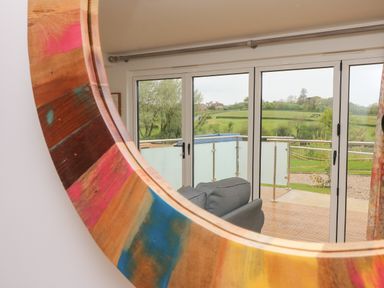 A glass door leading to a wooden balcony with a gray chair and a green field beyond at Syrah Seaview