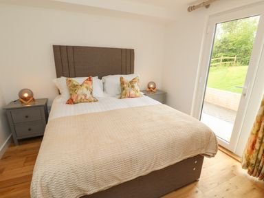 A bedroom with a double bed flanked by two gray bedside tables with lamps and a glass door showing a garden outside at Syrah in Seaview